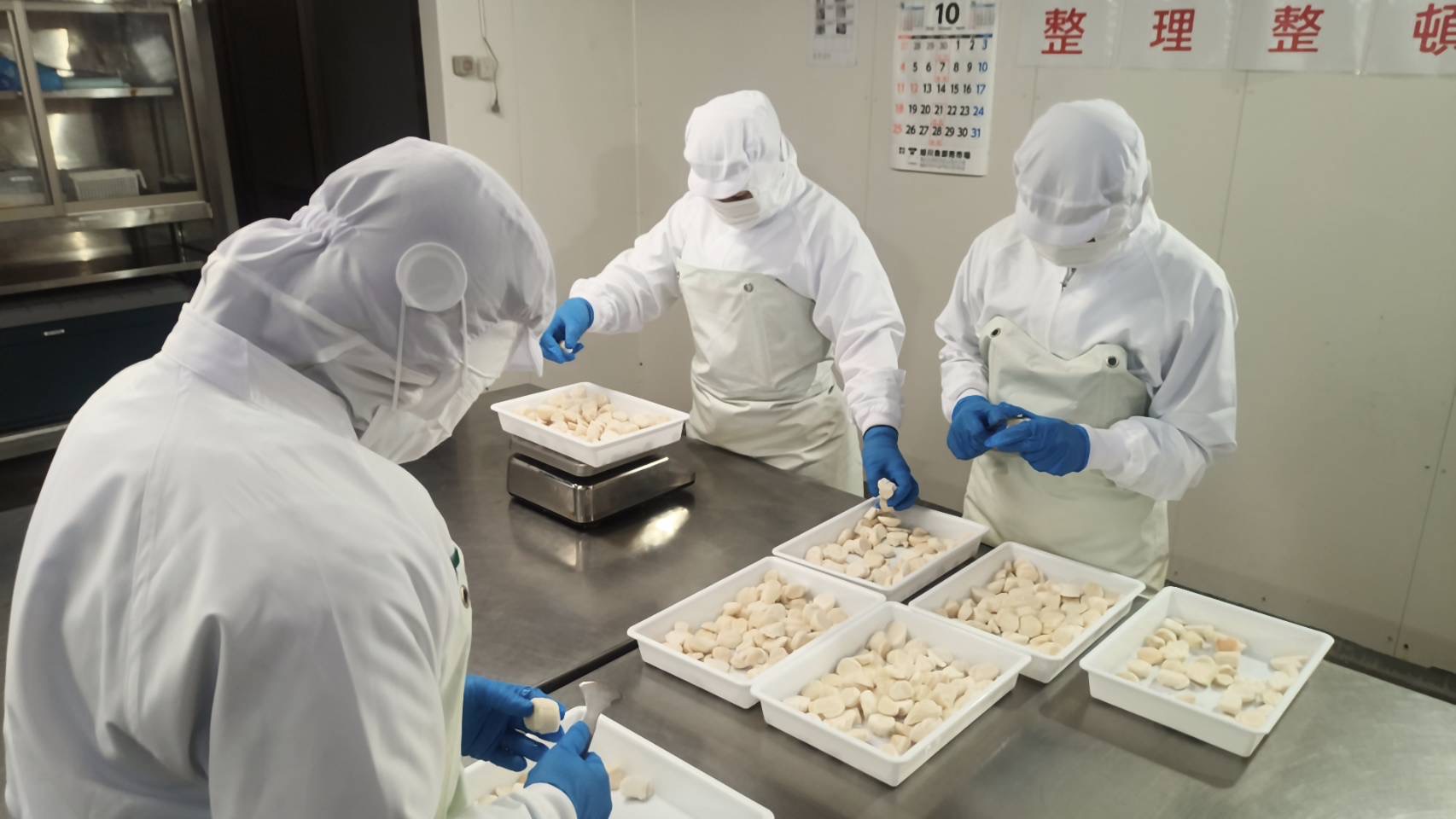 須永水産のスタッフが青い手袋でほたての貝柱を一粒ずつ扱う現場